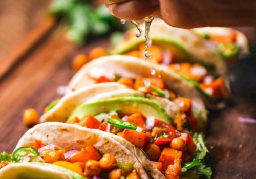 A hand squeezes lime over colorful tacos filled with chickpeas, vegetables, and fresh herbs, resting on a wooden board.
