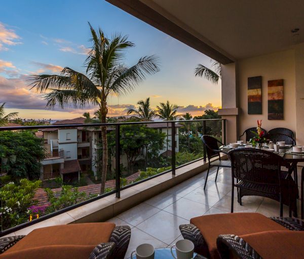 The image shows a cozy balcony overlooking a tropical landscape with palm trees and a picturesque sunset. It's inviting and serene.