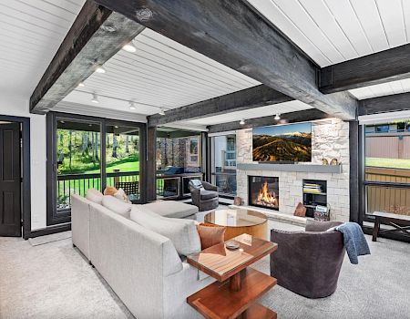 A cozy living room with modern furniture, a fireplace, and large windows overlooking a green yard completes the scene.