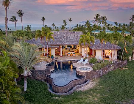 Luxurious tropical villa with a curved pool, palm trees, and a thatched-roof retreat, open-air living spaces, and lush garden surroundings.